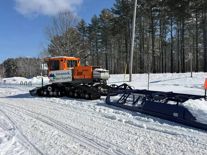 Greenstock Snow Sports groomer with club branding on a sunny winter day